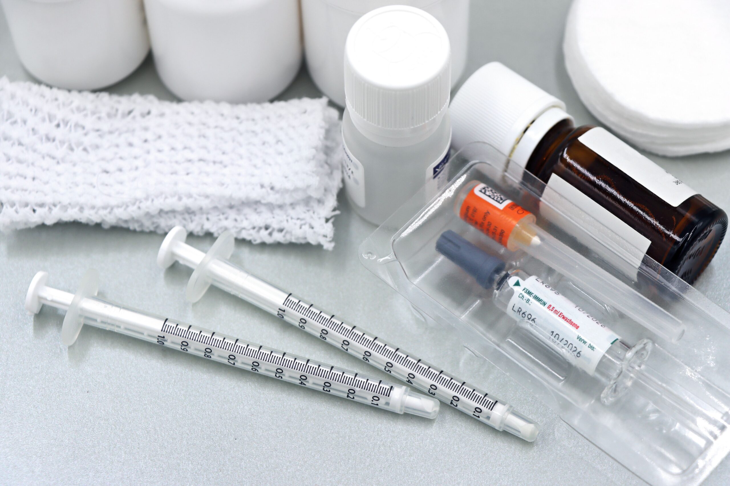Flat lay of medical tools and vaccines, including syringes and bottles, on a white surface.