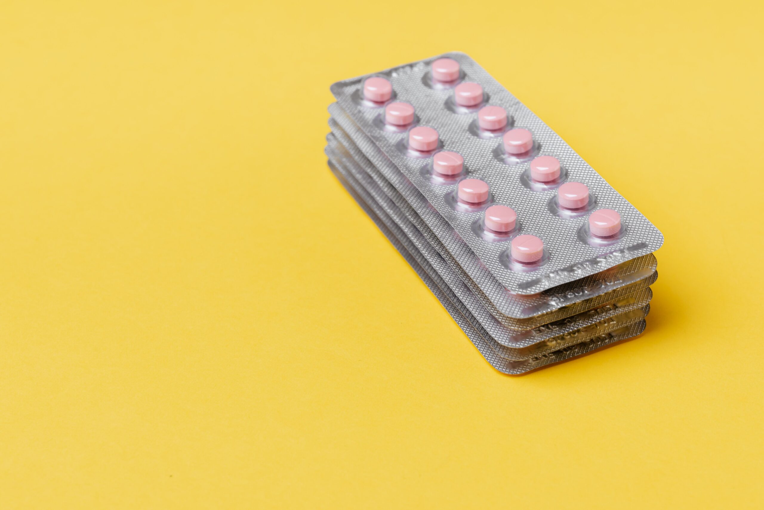 From above set of small round pink pills packed in blisters on top of each other on yellow surface