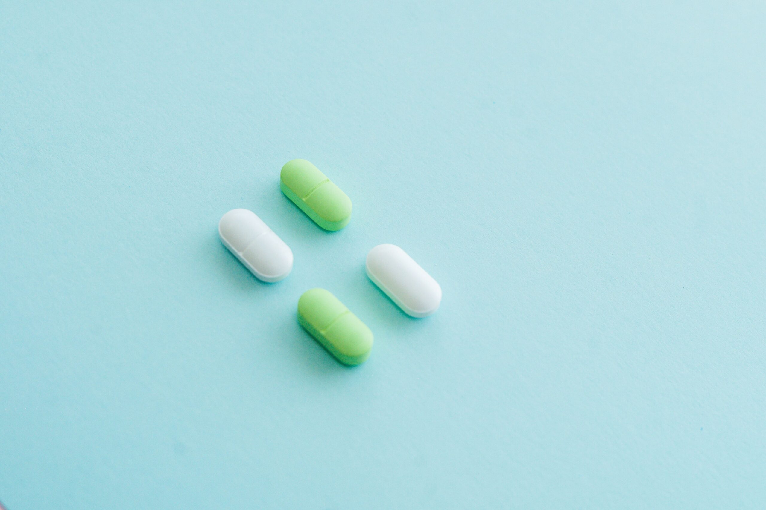 An assortment of green and white pills on a soothing blue surface.